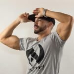 A man in a casual outfit striking a pose with his black cap against a neutral background.