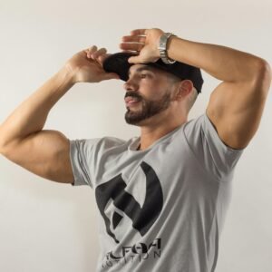 A man in a casual outfit striking a pose with his black cap against a neutral background.