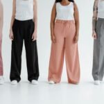 Four women stand in colorful trousers against a white background, showcasing diversity and fashion.