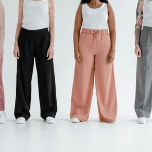 Four women stand in colorful trousers against a white background, showcasing diversity and fashion.