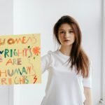 A woman stands indoors holding a colorful sign advocating for women's human rights.